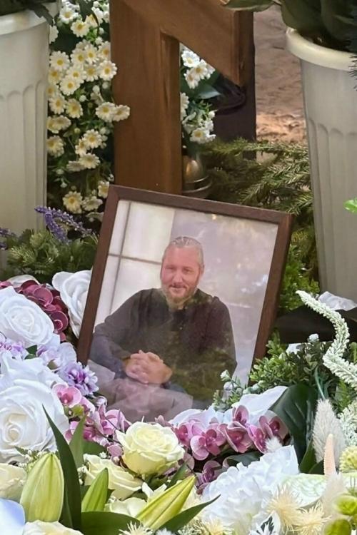 Максим сырников: деревянный крест, алые цветы и корчевников, вглядывающийся в портрет.

